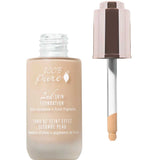 An open bottle of 100% Pure 2nd Skin Foundation 35ml with a dropper reveals beige serum foundation. The label features olive squalane and fruit pigments for a radiant, natural complexion.
