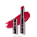 A shiny silver tube and cap with etched fruit designs holds the 100% Pure Lip Glaze 2.5g by 100% Pure, shown in a bright coral-pink shade with a lipstick bullet and matching swatch behind it. Text below reads Coraline.