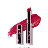 A tube of 100% Pure Lip Glaze 2.5g by 100% Pure labeled Rhubarb stands with its cap off, revealing the lipstick and a vibrant smear behind it. The metallic tube features decorative berry designs.