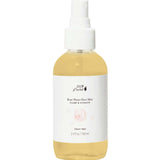 A clear spray bottle of 100% Pure Rose Water Face Mist 100ml, with a white cap, holds light yellow liquid. The label has a rose image and states it's a natural, vegan facial toner and makeup setting spray.