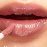 A close-up of lips being applied with 100% Pure Lip Gloss using a wand. Infused with vitamin E for hydration, the lips appear glossy and moisturized. The word Mauvely is in white at the bottom left corner.