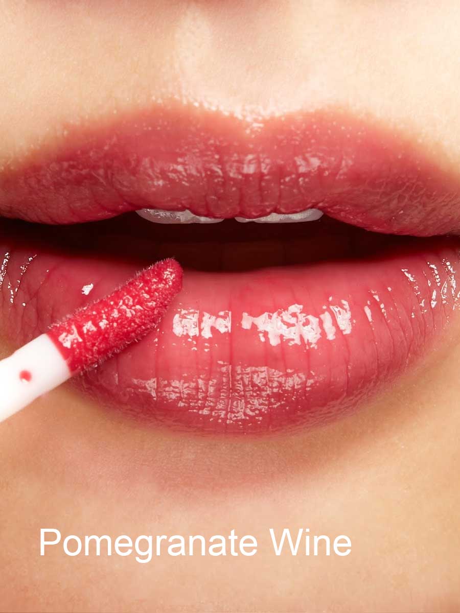 Close-up of glossy lips as a person applies 100% Pure Lip Gloss enriched with pomegranate oil using a wand applicator. The words Pomegranate Wine are written at the bottom of the image.