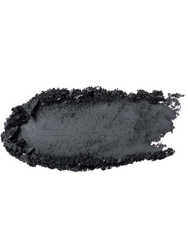 A close-up of a charcoal-black smear of 100% Pure Pressed Eye Shadow 2g by 100% Pure, with rough textured edges, displayed on a white background.