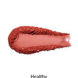 A swatch of 100% Pure Rice Powder Pressed Blush 9g in matte, dusty pink on a white background with "Healthy" below, demonstrating a natural flush and buildable coverage.
