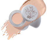 Open jar of 100% Pure Long Last Concealer in a light beige shade, featuring a floral lid design, displayed atop a swatch of concealer. The text "Alpine Rose" appears below.