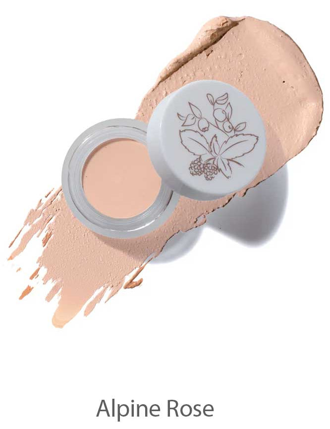 Open jar of 100% Pure Long Last Concealer in a light beige shade, featuring a floral lid design, displayed atop a swatch of concealer. The text "Alpine Rose" appears below.