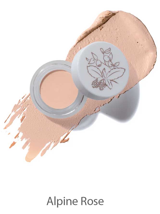 Open jar of 100% Pure Long Last Concealer in a light beige shade, featuring a floral lid design, displayed atop a swatch of concealer. The text "Alpine Rose" appears below.