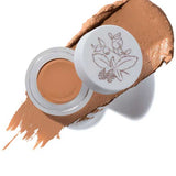 An open jar of 100% Pure Long Last Concealer 3g in a golden peach shade sits on a matching swatch, its lid adorned with a floral illustration. The text "Golden Peach" appears below.