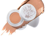 An open jar of 100% Pure Long Last Concealer 3g in Peach Bisque, with a white lid adorned by a botanical illustration. A swatch of the peach-toned, full coverage concealer is spread behind the jar. Text below reads "Peach Bisque.