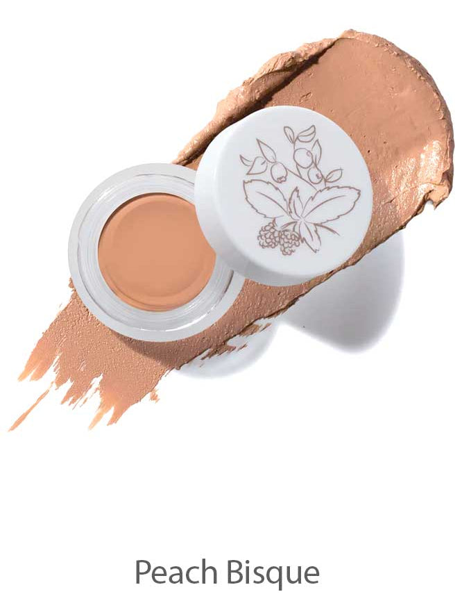 An open jar of 100% Pure Long Last Concealer 3g in Peach Bisque, with a white lid adorned by a botanical illustration. A swatch of the peach-toned, full coverage concealer is spread behind the jar. Text below reads "Peach Bisque.