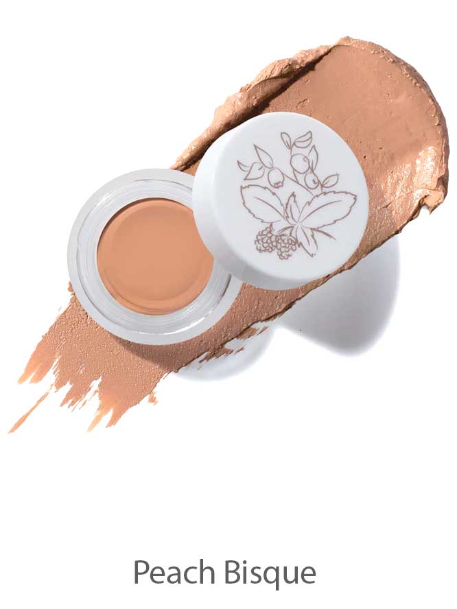 An open jar of 100% Pure Long Last Concealer 3g in Peach Bisque, with a white lid adorned by a botanical illustration. A swatch of the peach-toned, full coverage concealer is spread behind the jar. Text below reads "Peach Bisque.
