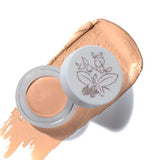 An open jar of 100% Pure Long Last Concealer with a floral lid rests on a beige smear, with the word “Crème” below.