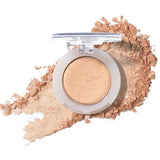An open compact of 100% Pure Pressed Eye Shadow 2g by 100% Pure in shimmery beige, with a light dusting of powder around it on a white background.