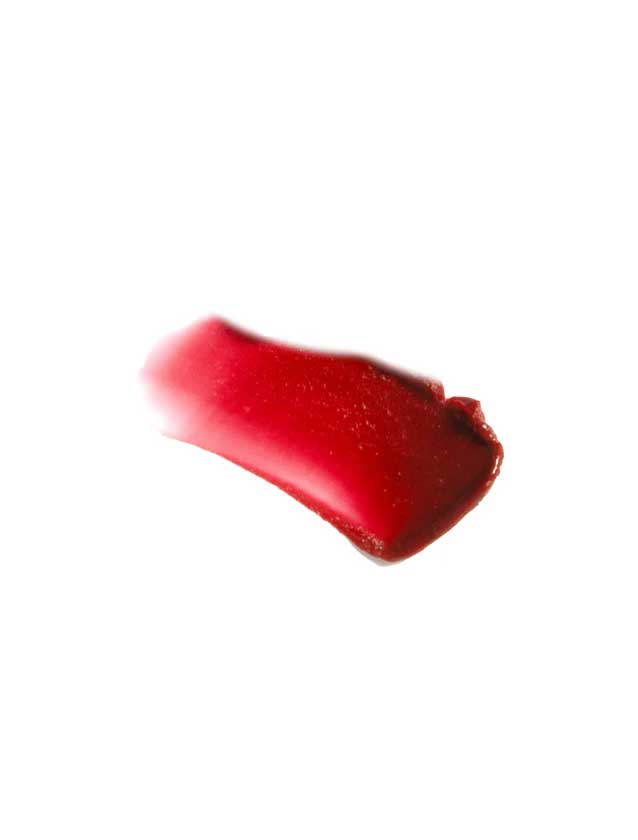 A swipe of 100% Pure Lip & Cheek Tint in Sugar Plum smears across a white background, revealing a rich berry hue with a glossy texture and subtly uneven edges.