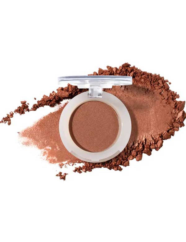 An open compact of 100% Pure Pressed Eye Shadow 2g by 100% Pure with a clear lid, shown on a white background with a swipe and scattered pieces of warm brown, natural mineral shimmer powder.