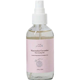 A clear spray bottle labeled "100% Pure Watermelon Cucumber Water Locking Mist 100ml" features a pink label, a white nozzle, and a watermelon illustration. The bottle contains 3.4 fl oz (100 ml).